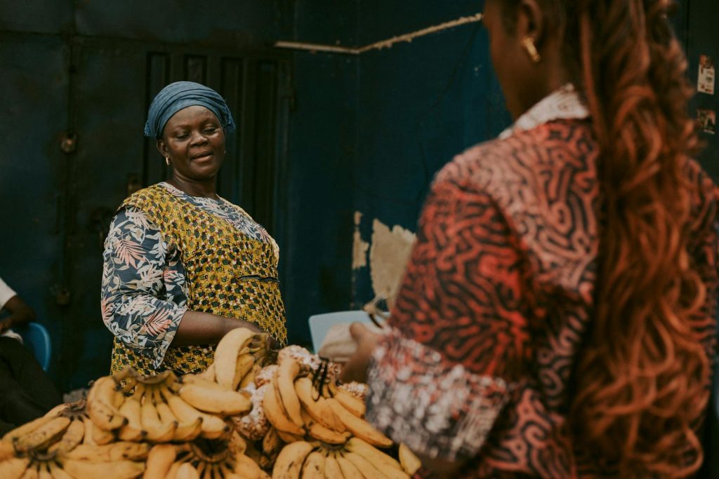 A vibrant African market scene showing a banana vendor interacting with a customer.