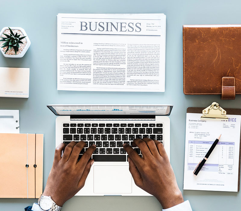 Brown notebook,, business newspaper, laptop and work documents on a table.